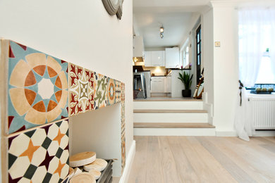 Immagine di un soggiorno design aperto con pareti bianche, parquet chiaro, cornice del camino piastrellata e camino classico