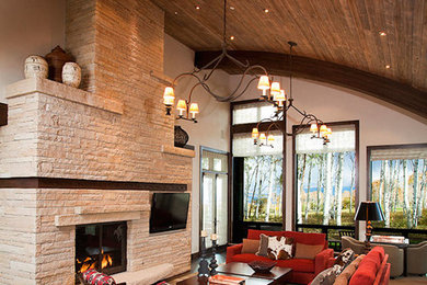 Modelo de salón abierto tradicional con suelo de madera oscura, chimenea de doble cara, marco de chimenea de piedra y televisor colgado en la pared