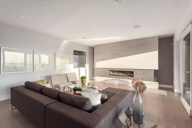 Cette photo montre un grand salon moderne ouvert avec un mur gris, un sol en bois brun, une cheminée ribbon, un manteau de cheminée en carrelage et aucun téléviseur.