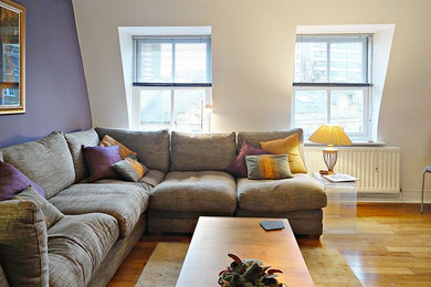 Trendy medium tone wood floor and brown floor living room photo in London with purple walls