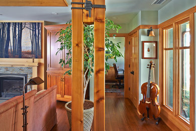 Modelo de salón con rincón musical abierto de estilo americano con paredes verdes, suelo de madera en tonos medios, todas las chimeneas y marco de chimenea de piedra