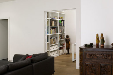 Modelo de salón abierto contemporáneo de tamaño medio con paredes blancas, suelo de madera clara y televisor colgado en la pared