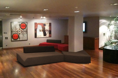 Ejemplo de salón tipo loft contemporáneo grande con paredes grises, suelo de madera en tonos medios, televisor colgado en la pared y suelo marrón