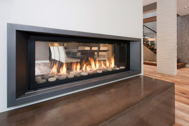 バンクーバーにある中くらいなトランジショナルスタイルのおしゃれなLDK (無垢フローリング、両方向型暖炉、金属の暖炉まわり、白い壁、壁掛け型テレビ、茶色い床) の写真