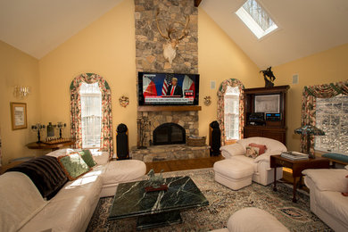 Ejemplo de salón abierto tradicional de tamaño medio con paredes beige, suelo de madera en tonos medios, televisor colgado en la pared, todas las chimeneas y marco de chimenea de piedra