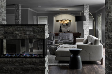 Mid-sized trendy brown floor and dark wood floor living room photo in Detroit with gray walls, a two-sided fireplace and a stone fireplace