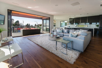 Modelo de salón abierto moderno grande con paredes blancas, suelo de madera en tonos medios y televisor colgado en la pared