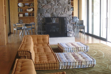 Imagen de salón abierto moderno grande con suelo de madera clara, chimenea de doble cara, marco de chimenea de piedra y televisor colgado en la pared