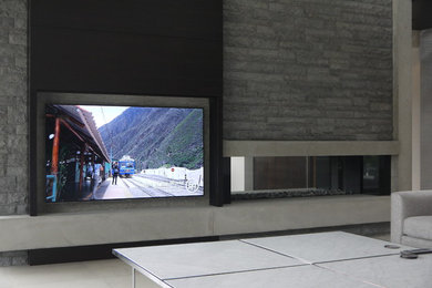 バンクーバーにある高級な中くらいなコンテンポラリースタイルのおしゃれなリビング (両方向型暖炉、石材の暖炉まわり、白い壁、コンクリートの床、内蔵型テレビ) の写真