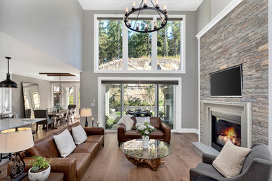 Example of a large transitional open concept medium tone wood floor and brown floor living room design in Other with gray walls, a standard fireplace and a wall-mounted tv