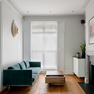This is an example of a contemporary formal enclosed living room in London with white walls, medium hardwood flooring, a standard fireplace and no tv.