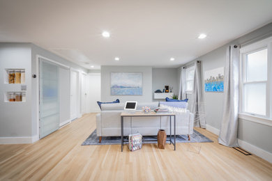 Modelo de salón para visitas abierto actual de tamaño medio sin chimenea con paredes grises, suelo de madera clara y televisor colgado en la pared
