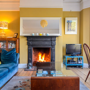 Eklektisches Wohnzimmer mit gelber Wandfarbe, braunem Holzboden, Kamin und freistehendem TV in Belfast