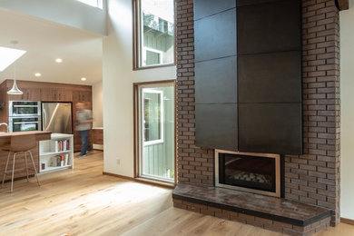 Inspiration for a contemporary living room in Seattle with a standard fireplace, a brick fireplace surround and brown floors.