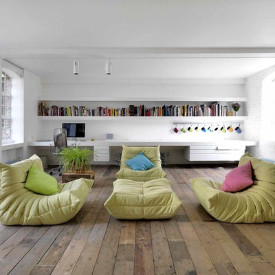 Living room library - industrial open concept medium tone wood floor living room library idea in London with white walls