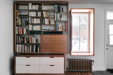 Modelo de biblioteca en casa abierta retro de tamaño medio con paredes blancas, suelo de madera en tonos medios y televisor colgado en la pared