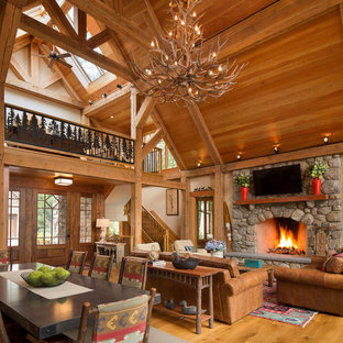 Example of a large mountain style formal and open concept medium tone wood floor and brown floor living room design in New York with beige walls, a standard fireplace, a stone fireplace and a wall-mounted tv