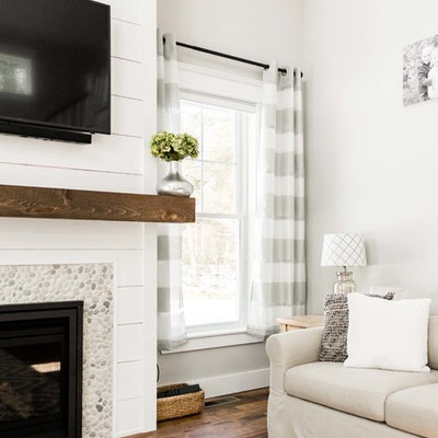 Inspiration for a large farmhouse enclosed medium tone wood floor and brown floor living room remodel in Portland Maine with gray walls, a standard fireplace, a stone fireplace and a wall-mounted tv