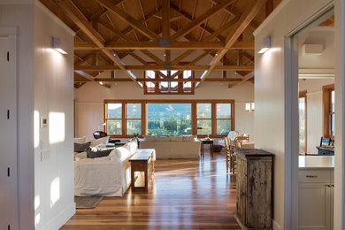 Modelo de salón abierto de estilo de casa de campo grande con paredes blancas, suelo de madera en tonos medios, estufa de leña, marco de chimenea de piedra y pared multimedia