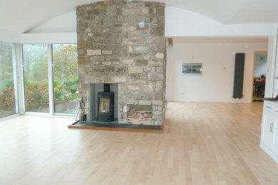 Ejemplo de salón abierto minimalista extra grande con suelo de madera clara, estufa de leña y marco de chimenea de piedra
