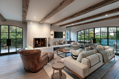 Example of a tuscan open concept light wood floor and beige floor living room design in Los Angeles with gray walls, a standard fireplace, a tile fireplace and a wall-mounted tv