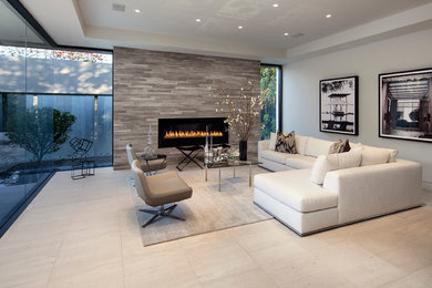 ロサンゼルスにある広いコンテンポラリースタイルのおしゃれなリビング (グレーの壁、トラバーチンの床、標準型暖炉、石材の暖炉まわり、テレビなし、ベージュの床) の写真