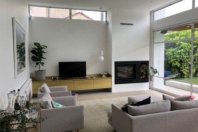 Imagen de salón abierto contemporáneo grande con paredes blancas, suelo de madera clara, todas las chimeneas, marco de chimenea de yeso, televisor independiente y suelo gris