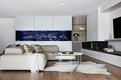 На фото: большая открытая гостиная комната в современном стиле с белыми стенами, паркетным полом среднего тона, телевизором на стене, коричневым полом, стандартным камином и фасадом камина из плитки с