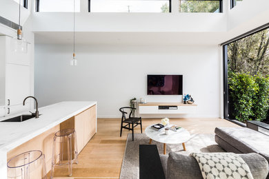 Imagen de salón abierto pequeño con paredes blancas, suelo de madera clara, televisor colgado en la pared y suelo beige