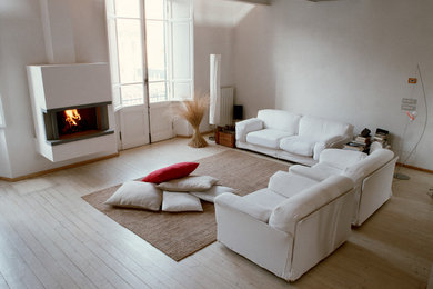Immagine di un soggiorno design con pareti bianche, parquet chiaro, camino lineare Ribbon e cornice del camino in intonaco