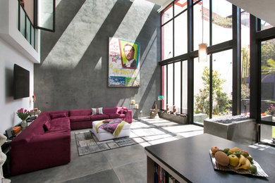 Modelo de salón abierto de tamaño medio con paredes grises, suelo de cemento, chimenea de doble cara, marco de chimenea de hormigón y televisor colgado en la pared