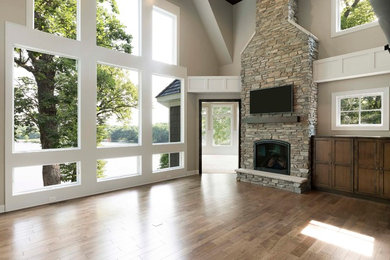 This is an example of a large rustic formal open plan living room in Minneapolis with beige walls, a standard fireplace, a stone fireplace surround and a wall mounted tv.