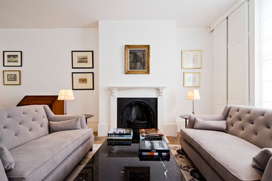 This is an example of a traditional open plan living room in London with white walls, medium hardwood flooring, a standard fireplace, a stone fireplace surround and a freestanding tv.