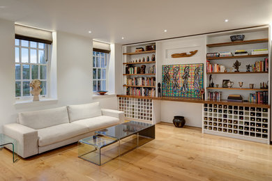 Ejemplo de salón para visitas abierto moderno grande con paredes blancas, suelo de madera clara y televisor retractable
