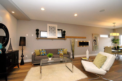 Mittelgroßes, Fernseherloses, Offenes Modernes Wohnzimmer mit grauer Wandfarbe, braunem Holzboden, Gaskamin, Kaminumrandung aus Metall und braunem Boden in Edmonton