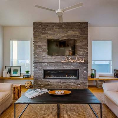 Example of a mid-sized trendy enclosed medium tone wood floor and brown floor living room design in Tampa with white walls, a standard fireplace, a stone fireplace and a wall-mounted tv