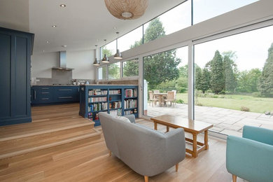 Cette image montre un grand salon design ouvert avec un mur blanc et un sol en bois brun.