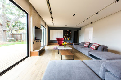 Foto de salón abierto contemporáneo de tamaño medio sin chimenea con paredes blancas, suelo de madera clara, televisor colgado en la pared y suelo beige