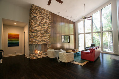 Großes, Repräsentatives, Offenes Modernes Wohnzimmer mit grauer Wandfarbe, dunklem Holzboden, Eckkamin, Kaminumrandung aus Stein und Multimediawand in Houston