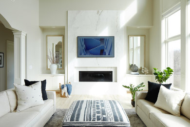 Modelo de salón abierto contemporáneo de tamaño medio con paredes grises, suelo de madera clara, todas las chimeneas, marco de chimenea de piedra y televisor colgado en la pared