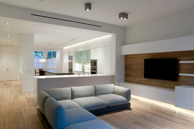 Diseño de salón abierto actual grande sin chimenea con paredes blancas, suelo de madera en tonos medios y televisor colgado en la pared