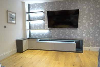 Modelo de salón abierto contemporáneo de tamaño medio con paredes grises, suelo de madera clara, televisor colgado en la pared y suelo marrón