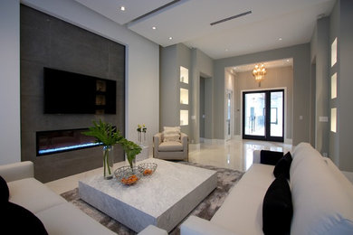 Modelo de salón contemporáneo con paredes grises, suelo de mármol, chimenea lineal, marco de chimenea de baldosas y/o azulejos y televisor colgado en la pared