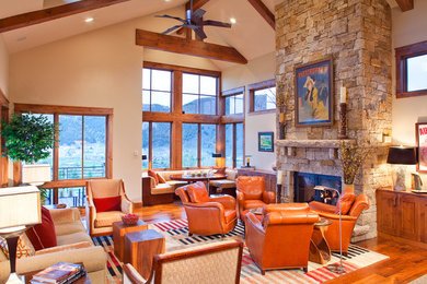 Large rustic open plan living room in Denver with beige walls, a stone fireplace surround, no tv, medium hardwood flooring, a standard fireplace, brown floors and feature lighting.