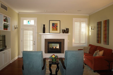 Modelo de salón cerrado de estilo americano pequeño con paredes amarillas, suelo de madera en tonos medios, chimenea de doble cara, marco de chimenea de madera y pared multimedia