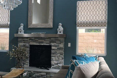 Modelo de salón contemporáneo con paredes azules, suelo de baldosas de cerámica, todas las chimeneas, marco de chimenea de piedra, televisor retractable y suelo gris