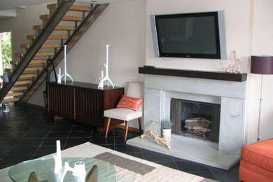 Diseño de salón abierto actual pequeño con paredes beige, suelo de pizarra, todas las chimeneas, marco de chimenea de hormigón, televisor colgado en la pared y suelo negro
