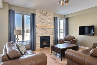 Ejemplo de salón abierto actual de tamaño medio con paredes beige, suelo de madera clara, todas las chimeneas, marco de chimenea de piedra y televisor colgado en la pared