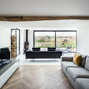 Diseño de salón actual, de tamaño medio, con paredes blancas, suelo de madera en tonos medios, estufa de leña, televisor independiente y suelo beige