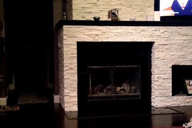 ロサンゼルスにある高級な中くらいなコンテンポラリースタイルのおしゃれなLDK (グレーの壁、竹フローリング、標準型暖炉、石材の暖炉まわり、据え置き型テレビ) の写真